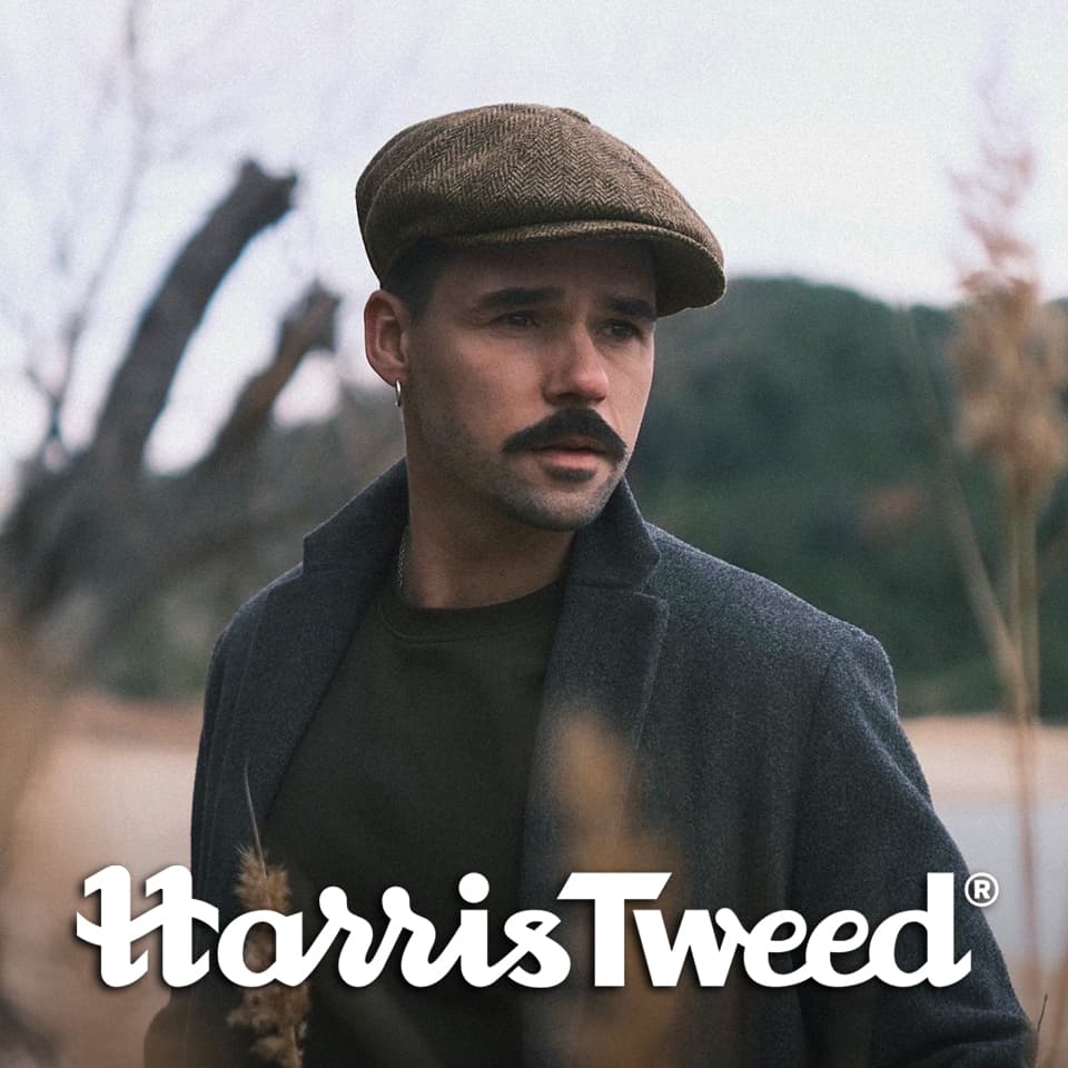 A man wearing a Harris Tweed newsboy cap by a river
